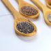 A variety of seeds and nuts in wooden spoons displayed on a white surface.