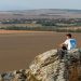 A man sits on a rock overlooking the vast countryside in a serene outdoor setting.